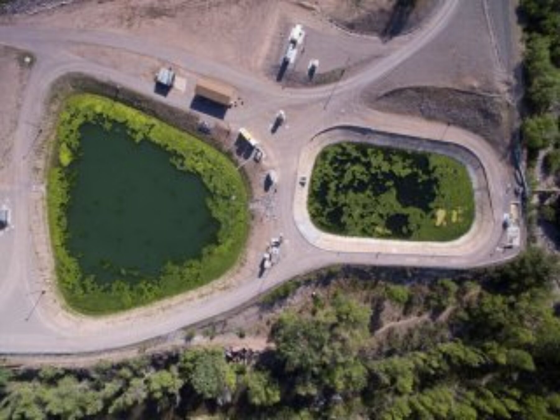 Aerial view of two wastewater treatment lagoons containing algae, service roads and a few buildings surround the lagoons in a climate with deciduous trees.