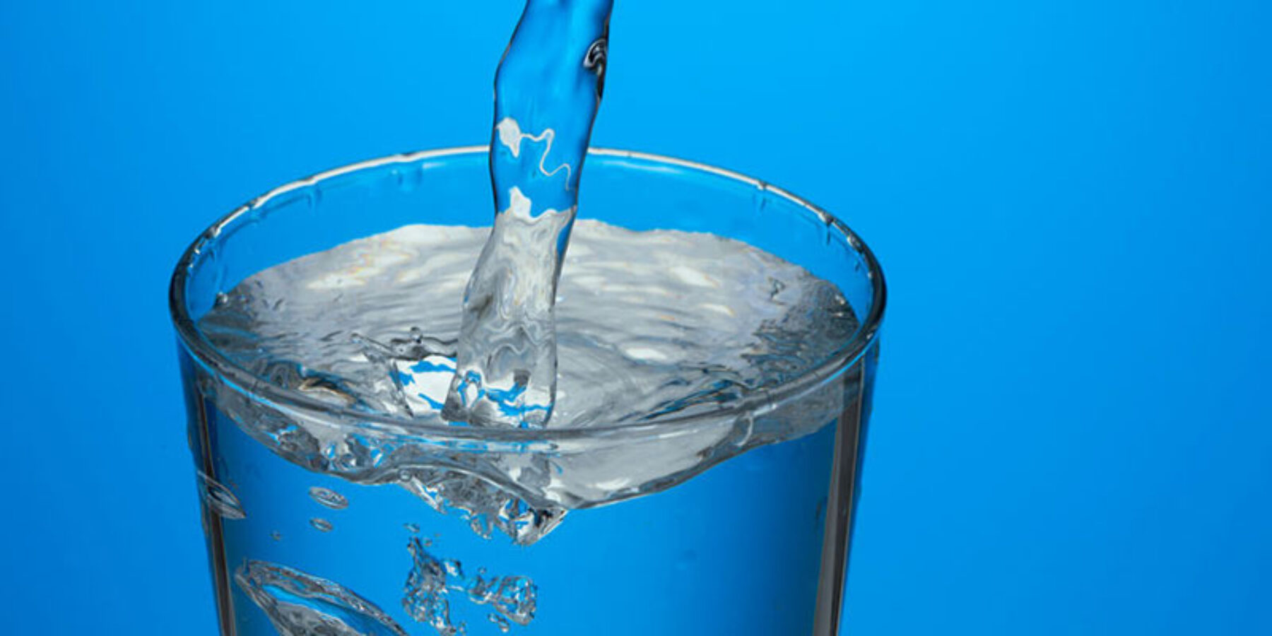 Water being poured into clear glass with a bright blue background